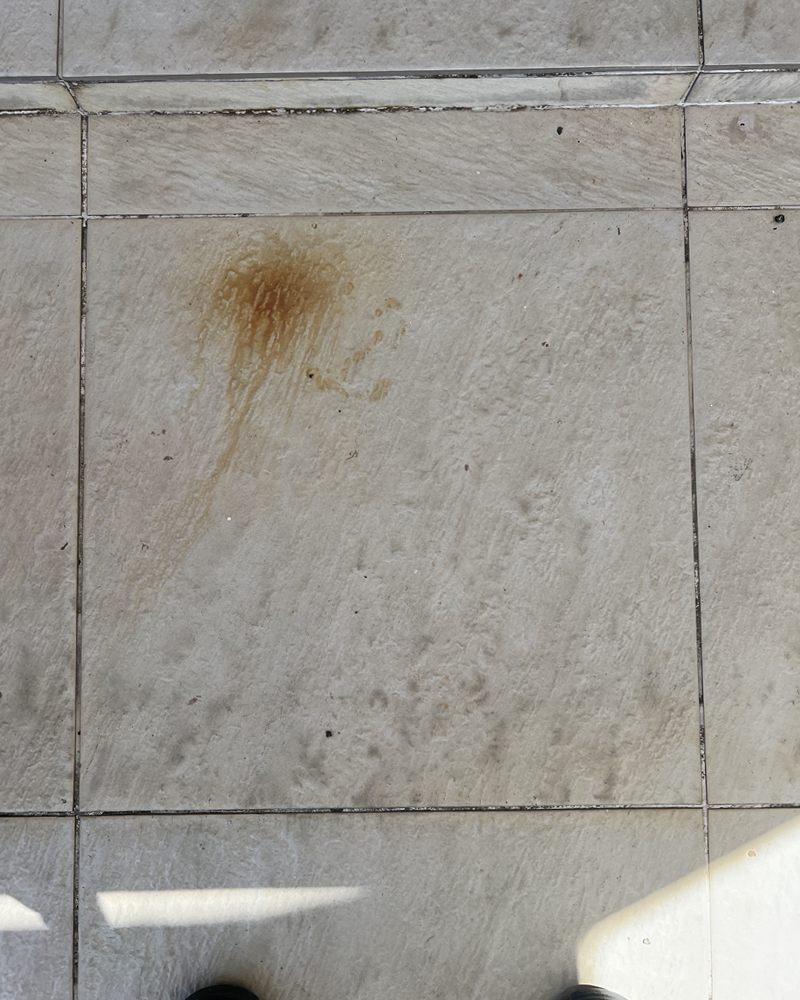 Piso cerâmico claro e texturizado com mancha de ferrugem e sujeira antes do serviço