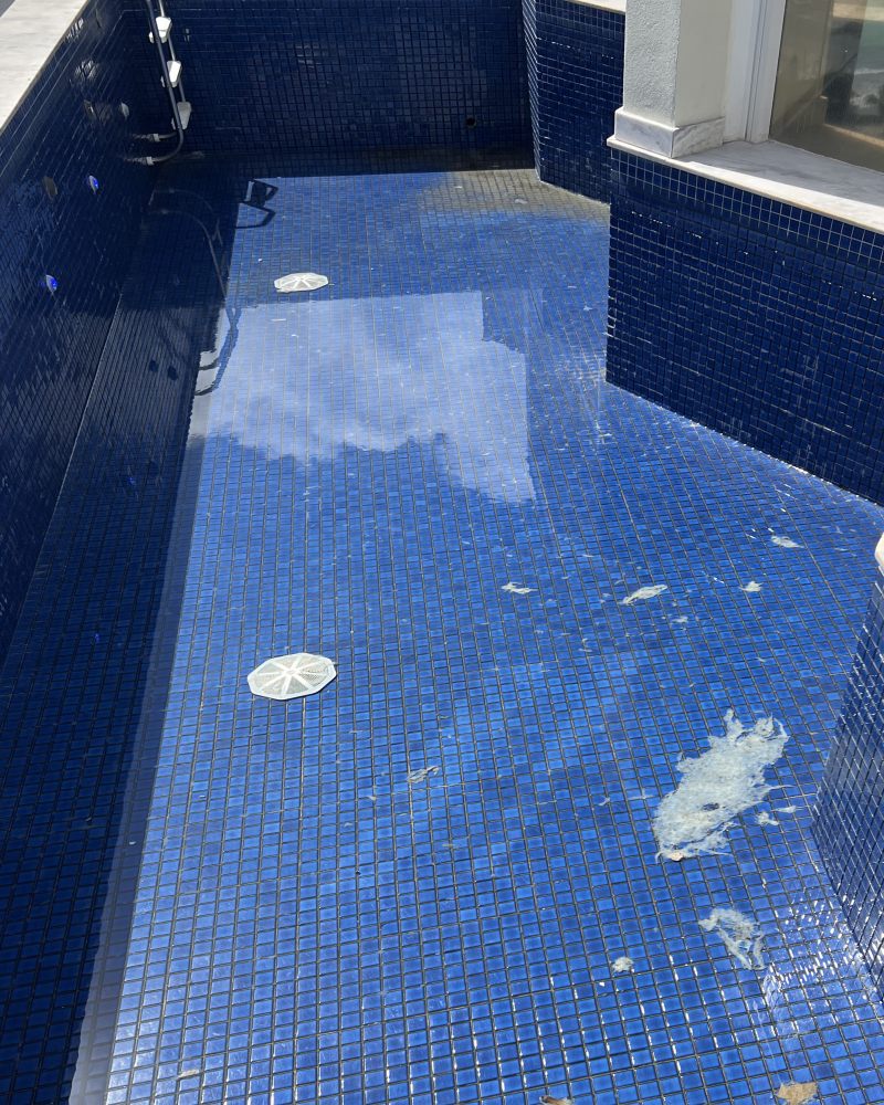 Piscina de pastilhas azuis com rejunte escurecido e sujeira no fundo antes do rejuntamento