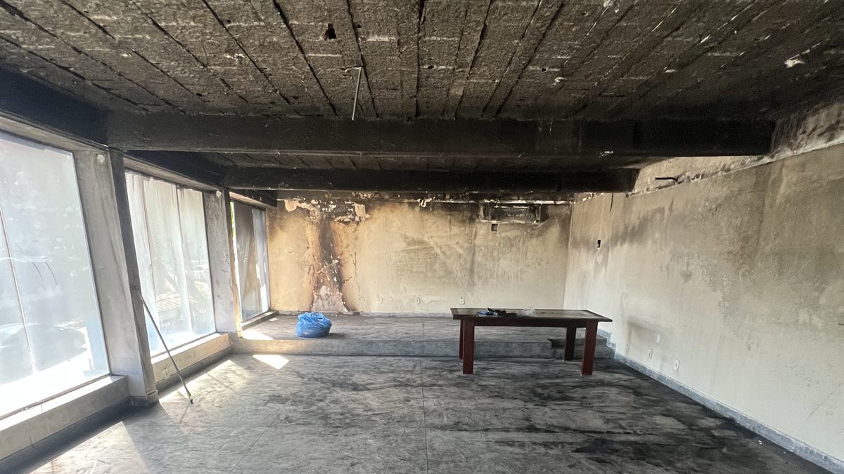 Salão comercial atingido por incêndio, com teto, vigas e paredes cobertos de fuligem