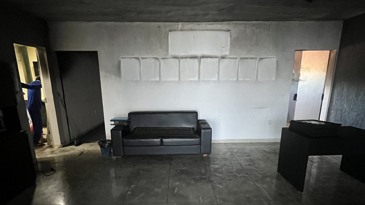 Sala com teto e paredes escurecidos pela fumaça e piso manchado de fuligem após um incêndio